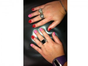 Duas mãos com as unhas pintadas de vermelho e rosa no estilo filha únia invertido.